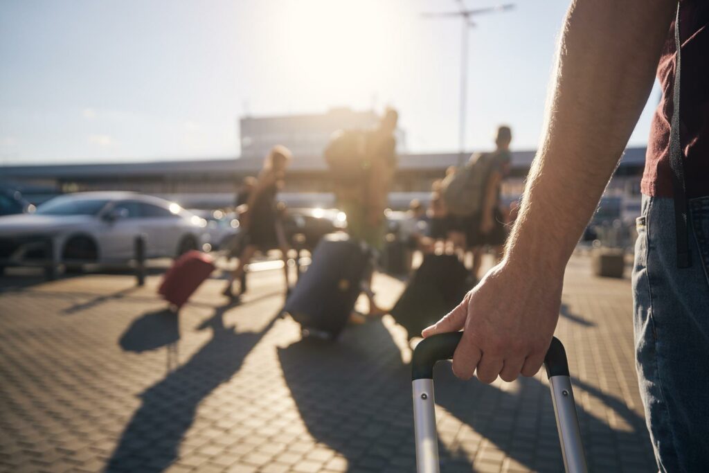 People walk through the parking lot at an airport with their rolling luggage